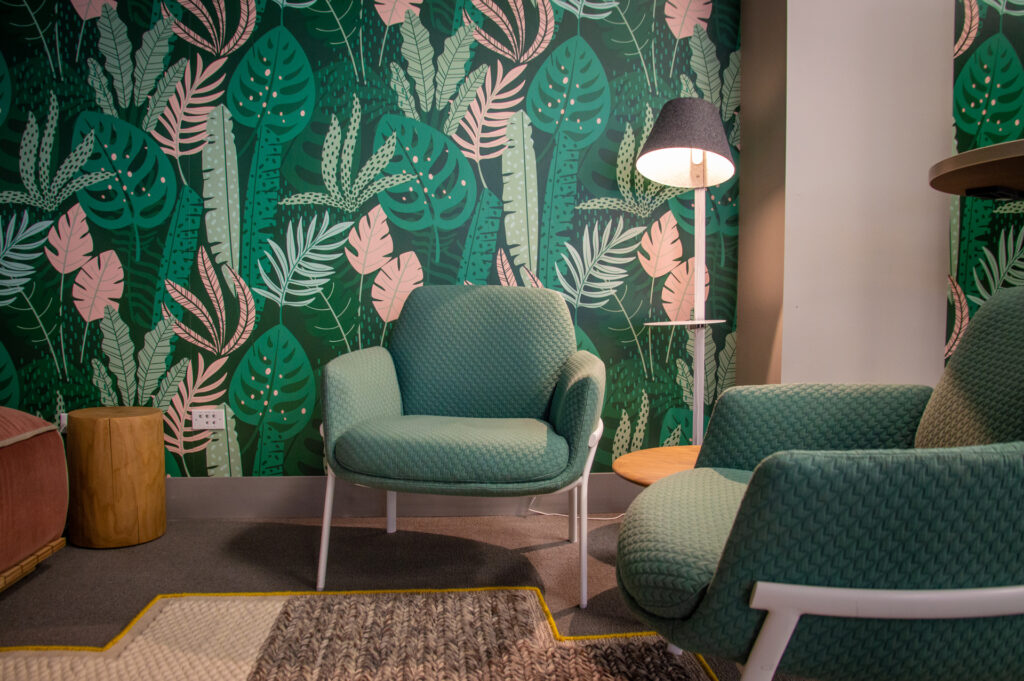 Botanical leaf-print wallpaper behind two sage green lounge chairs