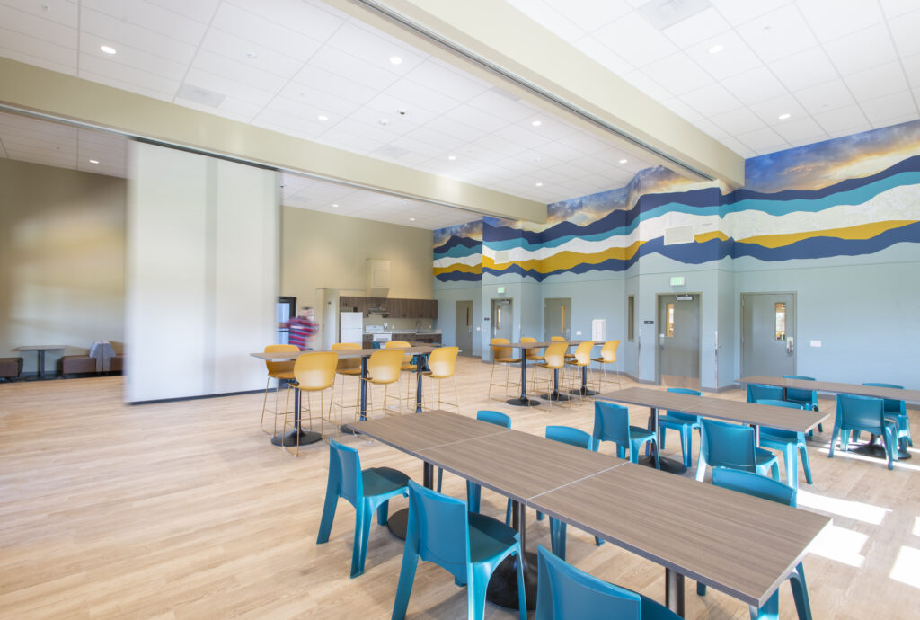 Community room with tables, stools and a mountain mural at the Idaho Youth Ranch Hands of Promise Campus