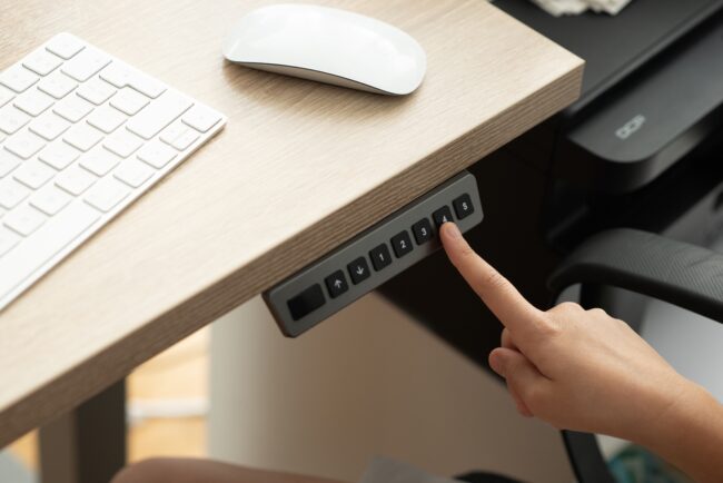 Human,Hand,Adjusting,An,Ergonomic,Electric,Desk,Or,Adjustable,Height How Height-Adjustable Tech and Lighting Impact Long-Term Employee Health