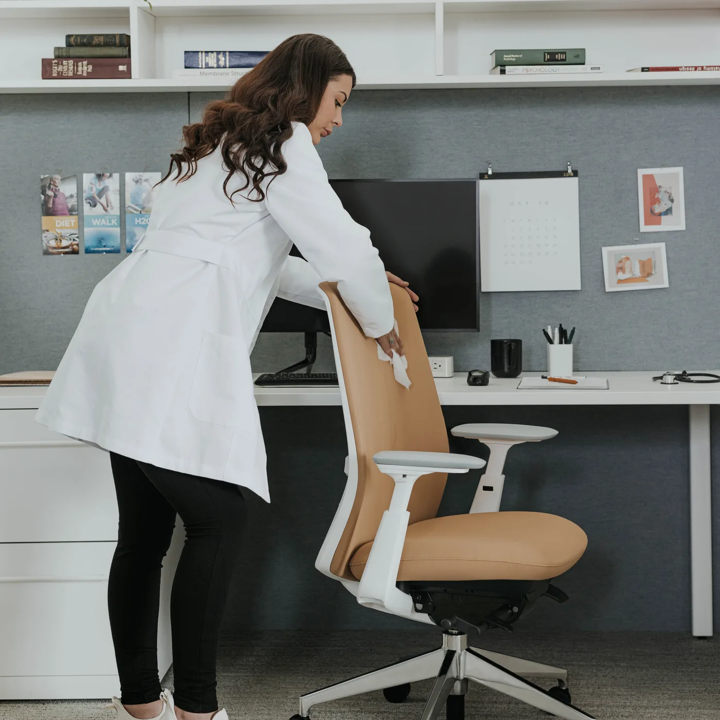 Caregiver in a lab coat wiping down a Soji Cleanable faux leather task chair at a clinical workstation
