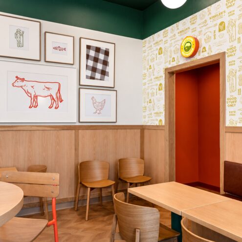 Kindler's dining area with wood chairs, gallery wall of framed prints and patterned wallpaper