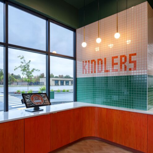 Kindler's order counter with orange casework, white and green tile wall and ordering kiosk by the windows