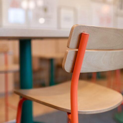 Close-up of an orange metal bar stool with a wood seat and back