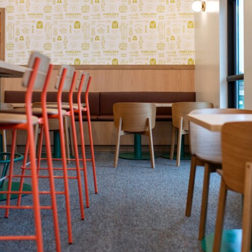Row of orange metal bar stools at a counter with wood chairs and bench seating along the wall