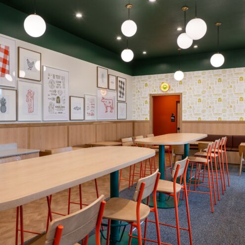Kindler's dining room with wood tables, orange bar stools, globe pendants and framed art under a dark green ceiling