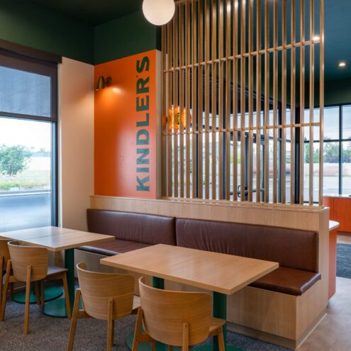 Kindler's booth seating with wood tables and chairs beside a slatted wood screen and orange accent wall
